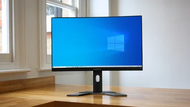 The Gigabyt G27QC 27in monitor, pictured on a table with a white wall and sash windows in the background