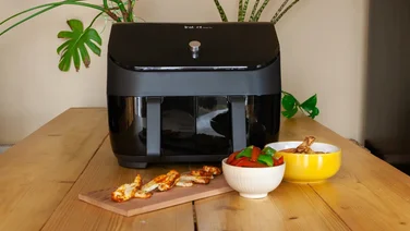 Article lead image depicting the Instant Vortex Plus Dual Drawer on a wooden table, with cooked chicken wings and peppers on a plate in front of it