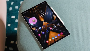 The Samsung Galaxy Tab S9 Plus offset against a blue background with its stylus and homescreen visible.