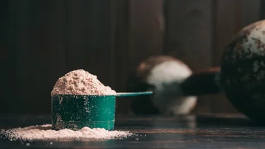 Best protein powder - Chocolate whey protein powder in measuring spoon, old rusty dumbbell on dark background. healthy eating, bodybuilding food supplements.