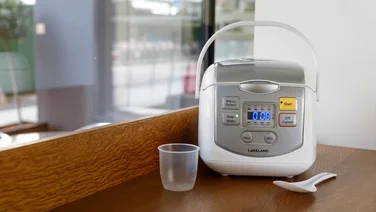 An image of a rice cooker on a table with a measuring cup and spoon