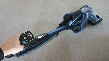 Image of a hand using a Shark vacuum cleaner from above on a beige carpet