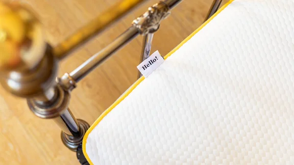 Corner of mattress with brass bed frame a "hello" tag