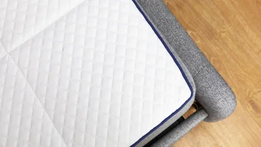 The corner of a white mattress, sitting on a grey bed frame