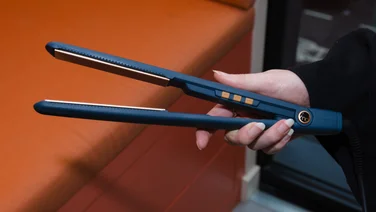 An image showing how we test hair straighteners. Woman's hand holding the straighteners in front of an orange background