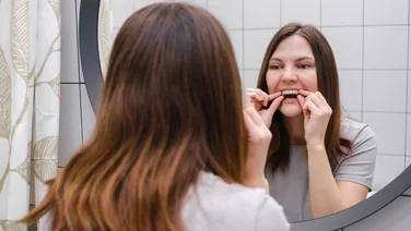 woman looking in the mirror to adjust her invisialign in a bathroom background