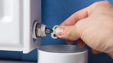 A close up of a persons hand using a radiator key to bleed their radiator