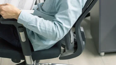 A man sits in an office chair leaning back reading some notes