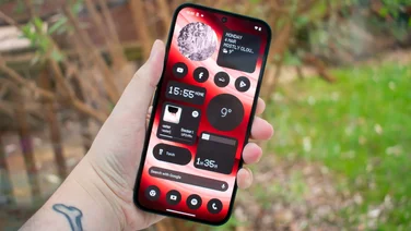Nothing Phone (2a) in hand, display showing home screen, in front of a window