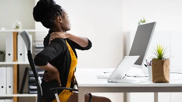 What does ergonomic mean - woman sitting uncomfortably in office chair, massages her shoulder