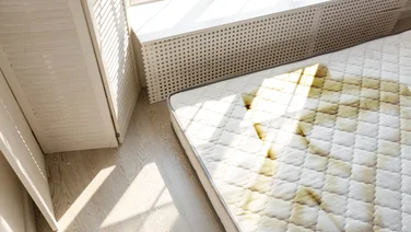 Why does my mattress smell -featured. A stained mattress on the floor in the corner of a brightly lit room.