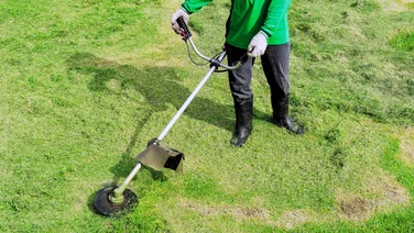 Lawn mower running costs explained - teaser - birds eye view of a person's torso and legs as they mow the lawn with a cordless electric lawn mower