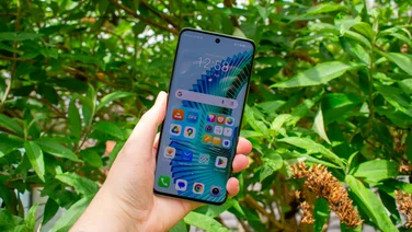 Front of Honor Magic 6 Lite being held in someone's hand with greenery in the background