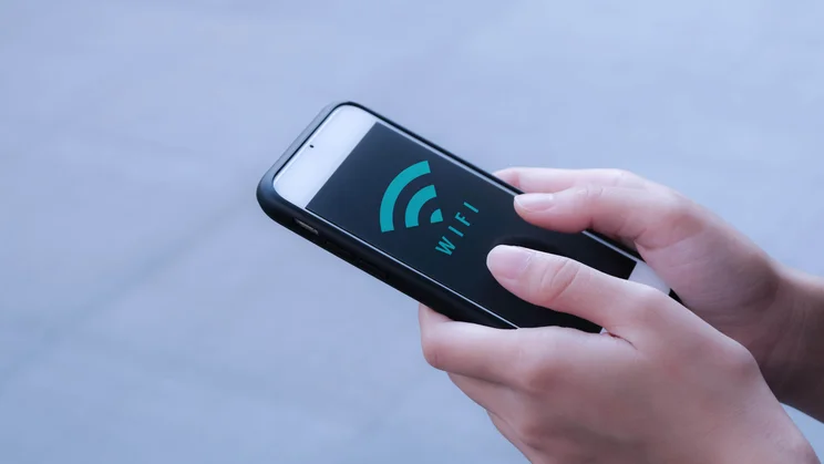 How to activate the hotspot on your iPhone - featured. Hands pointing phone with wi-fi symbol on screen upward