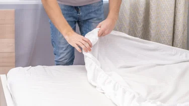 A man changes his white bedsheets