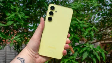 Samsung Galaxy A55 5G in hand, rear-view, in front of a green, leafy tree