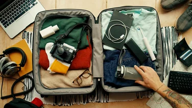 tattooed hand in suitcase moving and packing things - essential items to pack for travelling