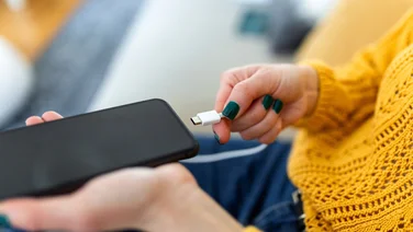woman in yellow jumper plugging in charger to phone lead - when should you charge your phone