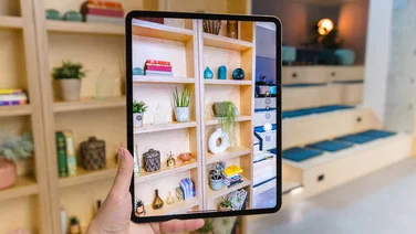A hand holds up the Apple iPad Pro (M4, 2024) in front of a bookcase