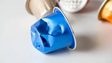 Are coffee pods bad for the environment - featured. Close up of a blue used coffee pod lying on a white surface with more pods in the background