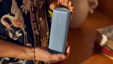 The Sonos Roam 2 in grey being held in two hands in a domestic setting