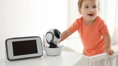 When to stop using the baby monitor - featured. A baby monitor camera and screen on a table in the foreground with a toddler in a crib in the background