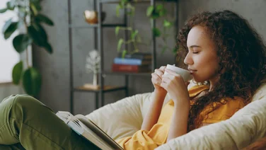 woman sitting on sofa in domestic setting sipping coffee - is coffee bad for you