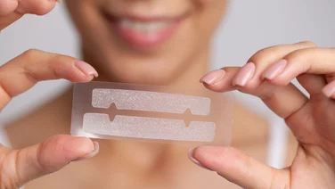 teeth whitening strips held close up with smiling woman in background - how often should you use teeth whitening strips