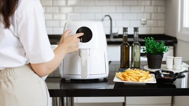 A woman selects a setting on an air fryer that's on a kitchen countertop