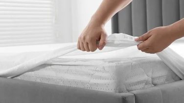 Do you need to use a mattress protector - featured. Close up of hands pulling mattress protector over a mattress