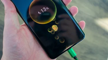 Honor Magic 6 Pro in hand, with a green cable plugged into the USB port, showing the charging progress on the screen