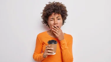 A woman in an orange top yawns while holding a beverage