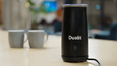 An image of the Dualit Handheld Milk Frother standing on a table next to two gray cups