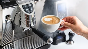 latte in mug being lifted by hand from espresso machine - this is why your espresso tastes bad