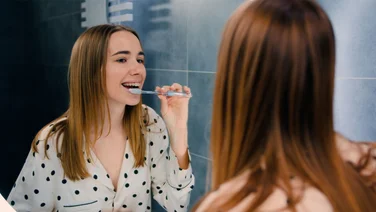 young girl brushing with braces in mirror and smiling - how to clean braces
