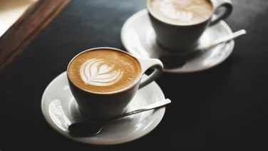 Pret's coffee subscription is ruined - featured. Two cups of cappuccino with latte art on black table.