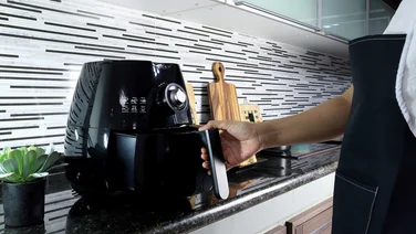 air fryer on counter with hand opening - air fryer vs halogen oven