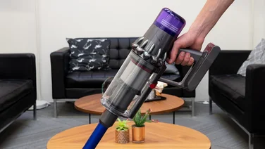 A persons hand uses the Dyson V11 to clean in a living room area