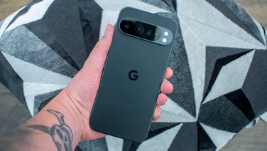 Google Pixel 9 Pro XL in hand, rear view, geometric grey cushion in the background