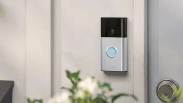 Ring Battery Video Doorbell mounted on a grey wall next to a door