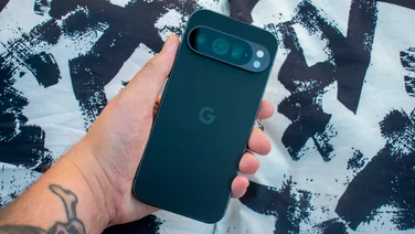 Google Pixel 9 Pro in hand, rear view, in front of black and white cushions