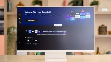 The Samsung M80D 32in monitor on a table with wood shelving in the background