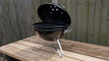 An image of the Weber Smokey Joe portable BBQ on an wooden table top outdoors