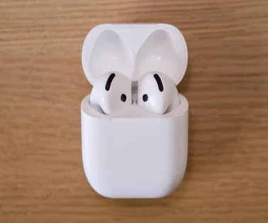 Apple AirPods 4 in the case with the lid open on a wood surface