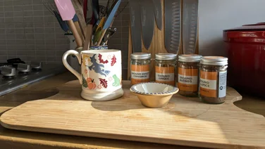 A coffee cup on a chopping board surrounded by small jars of various winter spices