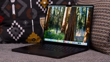 The Apple MacBook Pro 14in (M4, 2024) pictured on a grey sofa, open at a slight angle