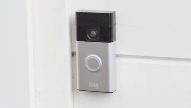 The Ring Battery Video Doorbell mounted on a pale yellow wood wall