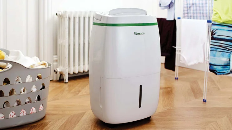A dehumidifier on the floor next to a clothes airer with clothes on it