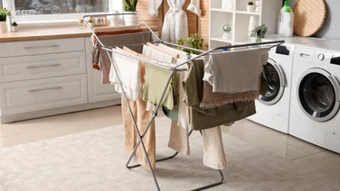 A picture of a clothes horse in a kitchen next to a counter and a washing machine and a tumble dryer