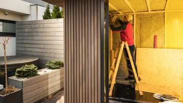 How to insulate a shed - lead image, lifestyle shot of man installing insulation in garden shed